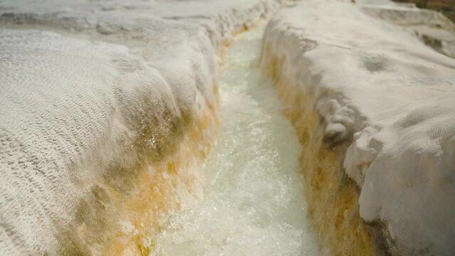 Calcite stalactites, a white stone channel resembling a canyon through which pure water flows from a spring, Pamukkale. In slow motion.