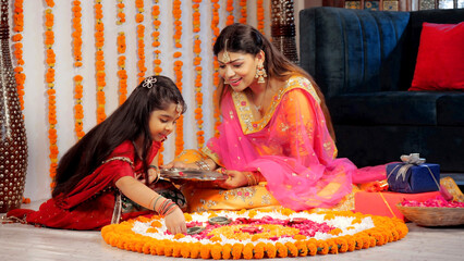 A loving mother and daughter decorating a traditional Rangoli with Diyas. Pretty female and her girl child sitting on the floor while decorating the house for Diwali celebrations - a Hindu festival...