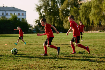 Full length photo of kids, football players in sport uniform training in motion with ball before...