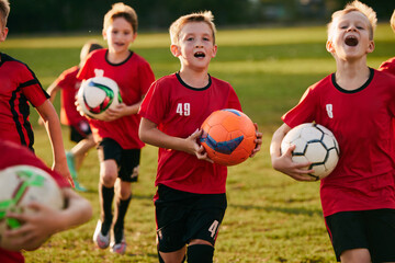 Close up portrait of kids soccer players running holding balls on sport, football field on match in motion. Playing football. Children's team games.