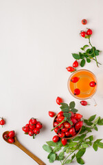 Cup with rosehip drink, bowl with rosehip berries, rosehip branches, berries in a wooden spoon on a light background.Composition with rose hips free space for writing