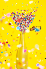 Confetti popping champagne bottle on yellow background