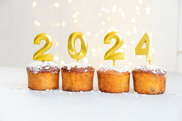 Golden candles with 2024 number on top of cupcakes with Christmas lights on background. Merry Christmas and Happy New Year celebration mood. Happy holidays. Festive pastry dessert.