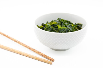 Wakame Seaweed in a white bowl Isolated on White Background with chopsticks on its side.