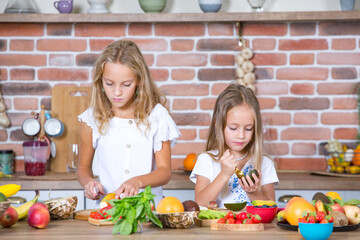 Two little girls in the kitchen with fresh vegetables. Healthy food concept. Happy sisters.