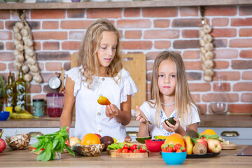 Two little girls in the kitchen with fresh vegetables. Healthy food concept. Happy sisters.