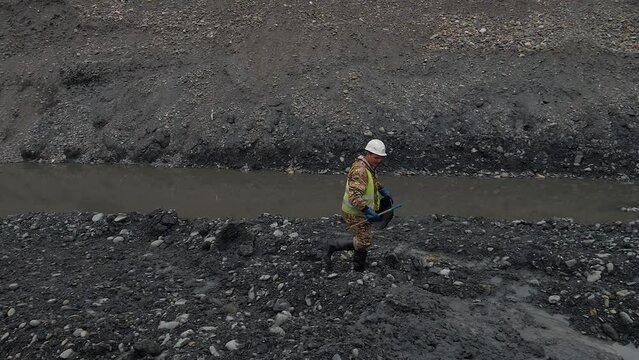 Surveyor worker uses a pan for gold mining at the quarry. Surveyor searching for gold in the dirty water at the open-pit mine. Surveyor mining for precious metals using gold panning method.