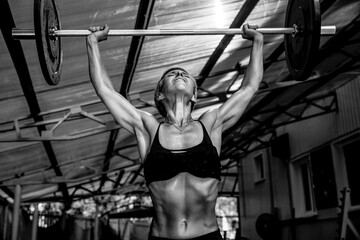The woman bodibilder raises the barbell in the gym.