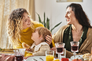 joyful lesbian couple and toddler child enjoying delicious dinner while gathering on Thanksgiving