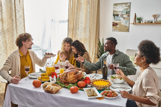 Happy Man Passing Plate With Roasted Potatoes To African American Friend During Thanksgiving Dinner