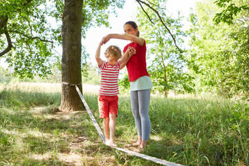 Mother assisting son doing slacklining in garden