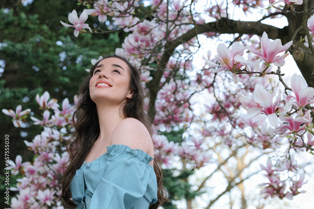 Poster Beautiful woman near blossoming magnolia tree on spring day