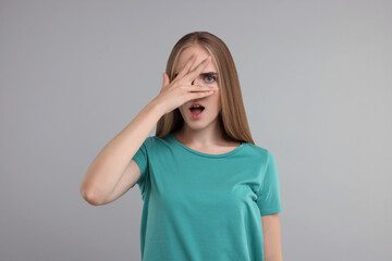 Embarrassed woman covering face with hand on grey background