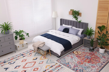 Stylish bedroom with double bed and beautiful green houseplants, above view. Modern interior
