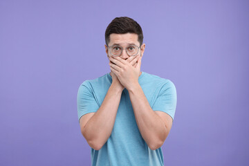 Embarrassed man covering mouth on purple background