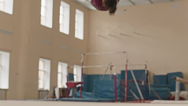 Slowmo of dedicated Biracial girl performing three somersaults one after another while preparing for artistic gymnastics championship in studio