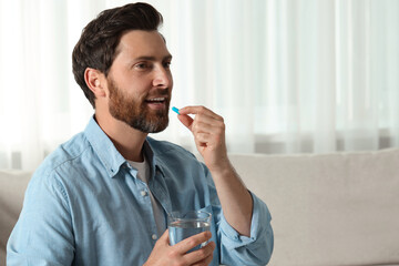 Handsome man with glass of water taking pill at home, space for text