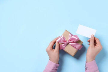 Woman with gift box and blank card on light blue background, top view. Space for text