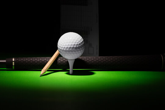 Golf Ball Pencil and Club Handle grip with score card in the distance,  golf equipment on a black and green background