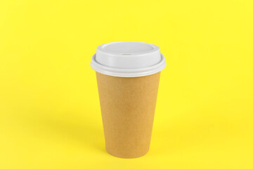 Paper cup with plastic lid on yellow background. Coffee to go