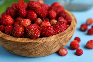 Fresh wild strawberries in bowl on light blue table, closeup