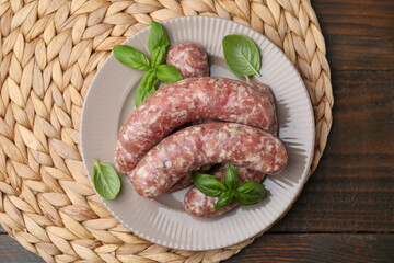 Raw homemade sausages and basil leaves on wooden table, top view