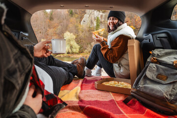 couple sitting in car trunk having picnic resting at nature