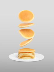 Many fresh pancakes falling onto plate against light grey background