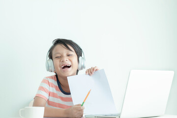 Happy Asian kid holding a piece of paper and laughing while learning online with a laptop