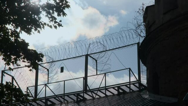 Prison tower and high fence with barbed wire. The sun's rays penetrate through the fence.