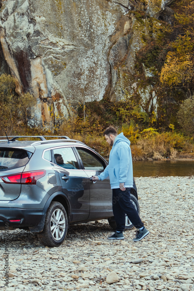 Wall mural man car traveler stop at river rocky beach enjoying the autumn forest