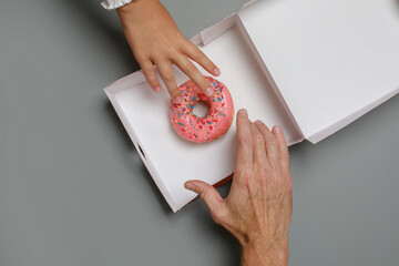 Colorful pink donut and human hands close up on board table, top view