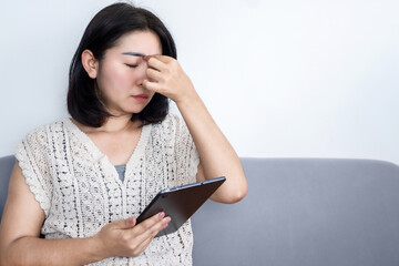 Asian woman suffering from eye pain watching too much on tablet screen because of blue light