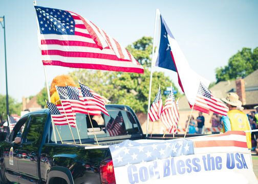 God bless the USA banner rear modern pickup truck dense of American flag on cargo bed driving on residential street smalltown Fourth of July parade, Dallas, Texas, USA blurry people