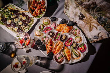 Assorted snacks, delicious meat, vegetables, bread, pita and sweet dishes on dark background, top view, toning