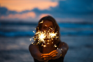 Young woman holding sparkler celebrating new years eve on the beach - Powered by Adobe