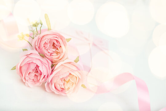 Three pink roses with ribbon and giftbox on the white table