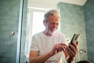 Senior man using a smartphone in the bathroom at home