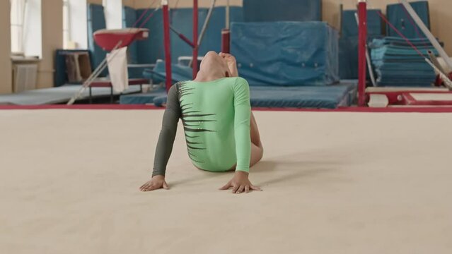 Concentrated Caucasian little girl in leotard doing elegant floor routine of artistic elements while practicing gymnastics in spacious class