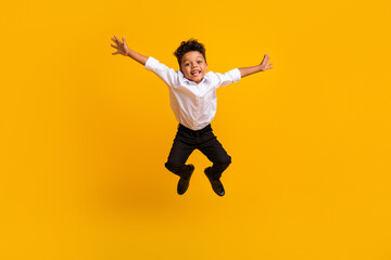 Full size photo of optimistic active schoolboy with curly hair dressed white shirt jumping having fun isolated on yellow color background