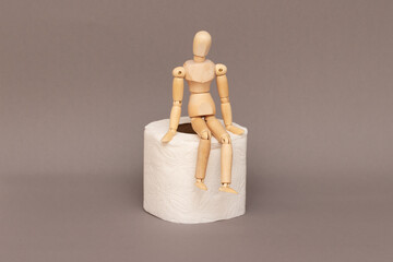 A wooden mannequin sits on a roll of toilet paper, demanstrating problems with defecation.