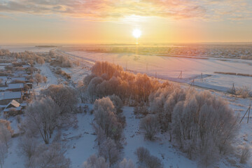 Winter dawn over snow-covered fields and trees in frost