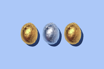 Three gold and silver foil wrapped chocolate easter eggs, as a holiday background.