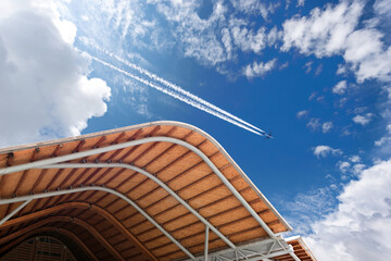 Airliner with contrails flying above a modern airport against a beautiful cumulus clouds or...
