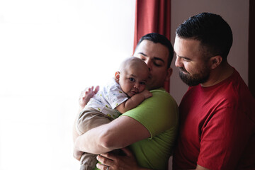 Couple of a husband and wife holding their adopted child close to the window, bringing colic out...