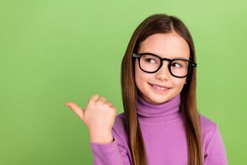 Portrait of cheerful smart schoolgirl dressed pullover in glasses look directing at sale empty space isolated on green color background