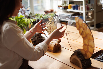 Blurred asian florist putting modern herbarium in glass frame in wooden stand in floral shop
