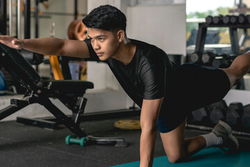 A young handsome asian man does a set of Bird-Dogs on a mat at the gym. Doing simple core exercises.