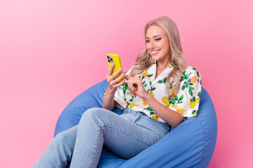 Photo of positive young girl blonde wavy hair use smartphone sitting blue beanbag check her wishlist ebay isolated on pink color background