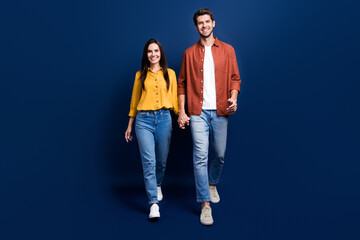 Full body portrait of cheerful peaceful two people hold arms walking isolated on dark blue color...